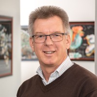 portraitfoto-carsten-koch Auf dem Bild ist Carsten Koch zu sehen. Er lächelt und trägt eine Brille sowie einen braunen Pullover.
